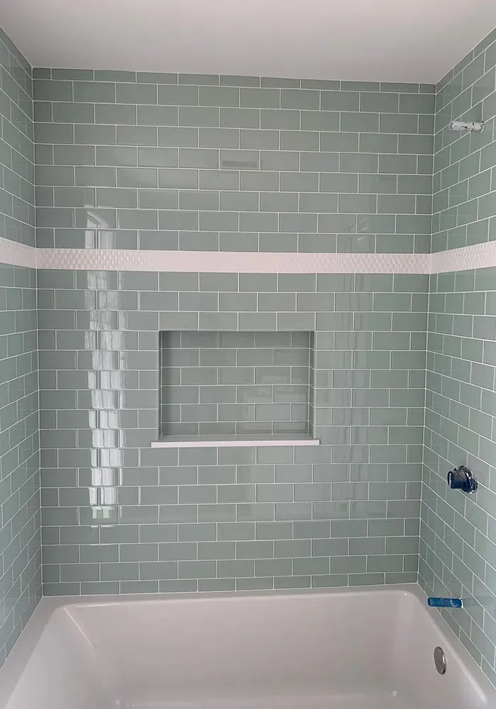 Pale green subway tile bathtub surround with a recessed niche