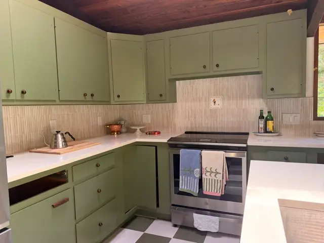 Sage green cabinets with a textured tile backsplash behind a stainless range