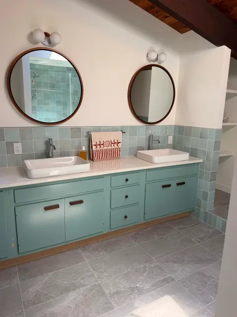 Blue-green double vanity with round wood-framed mirrors and a quartz countertop