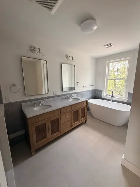 Wood vanity with round mirrors beside a freestanding tub by a bright window