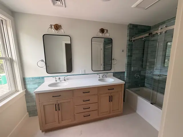 Wood double vanity beside a sliding barn-door glass shower enclosure