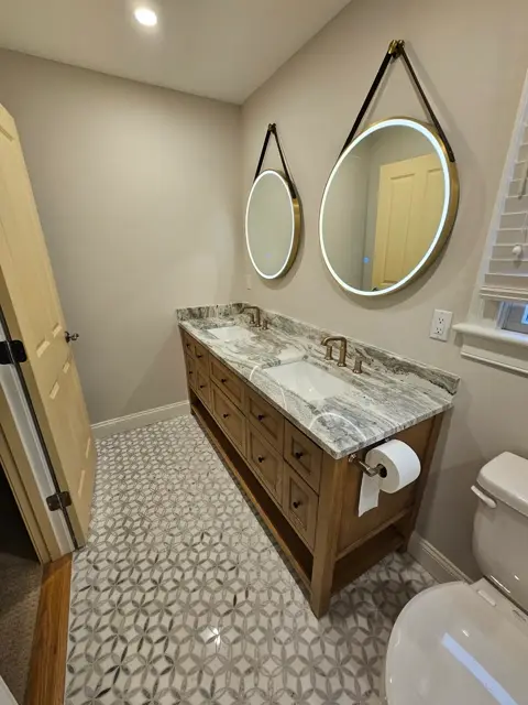 Round hanging mirrors over a marble-top vanity with patterned floor tile