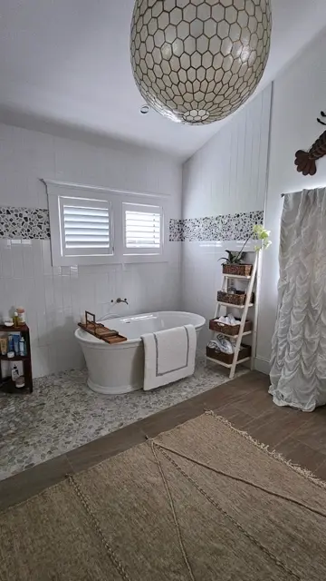 Freestanding tub under a capiz shell pendant light with a pebble tile floor