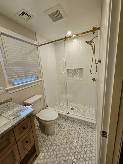 Frameless shower with brushed gold fixtures over a hexagon tile floor
