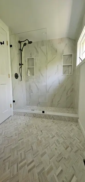 Frameless glass shower with black hardware over a herringbone floor