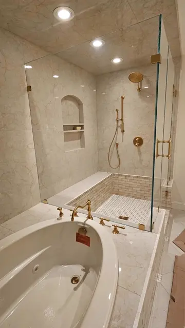 Frameless glass shower and tub finished in marble tile with brass fixtures